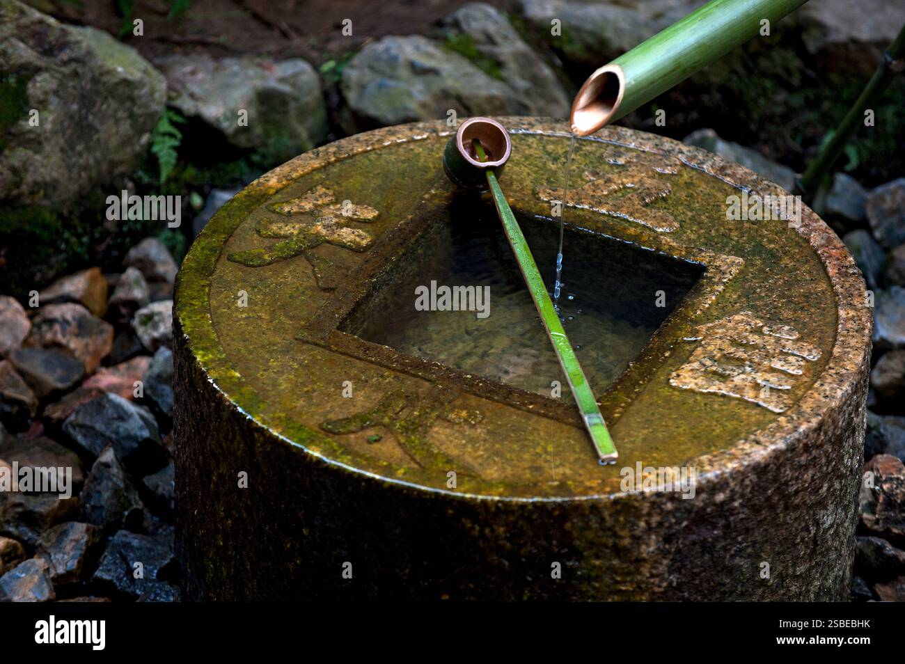 Old coin-shaped 'tsukubai' (round stone water basin) with 'hishaku' bamboo ladle in garden at Ryoanji Zen Temple in Kyoto, Japan. Stock Photo