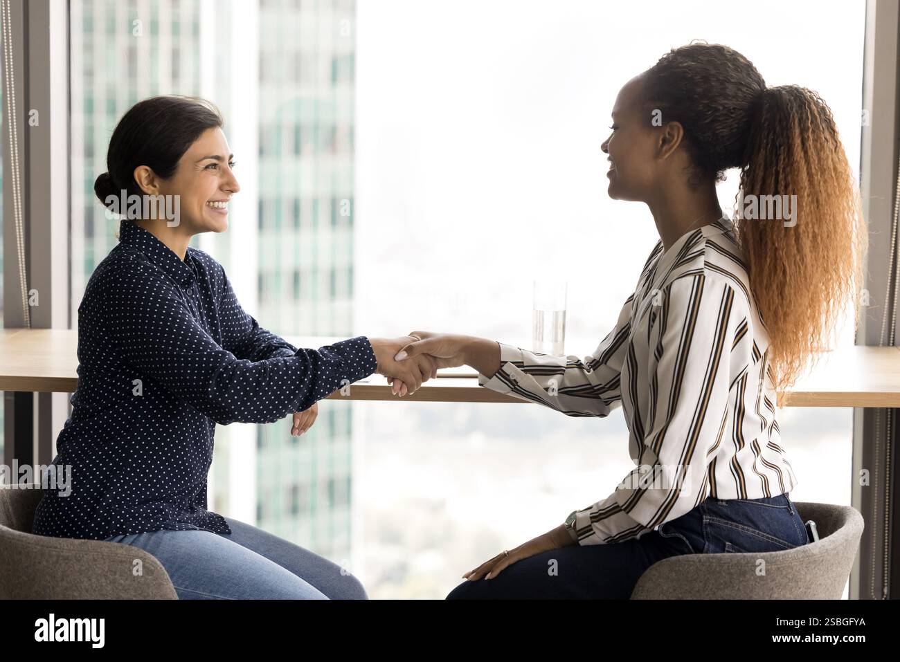 Two women shaking hands in modern office Stock Photo