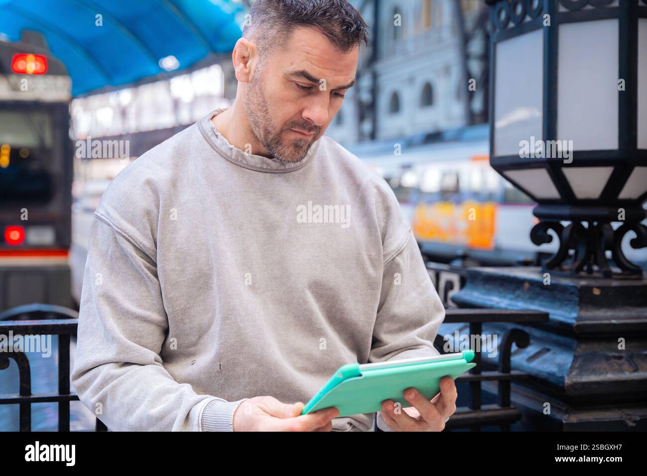 Focused Man Using Tablet While Waiting at Train Station Stock Photo