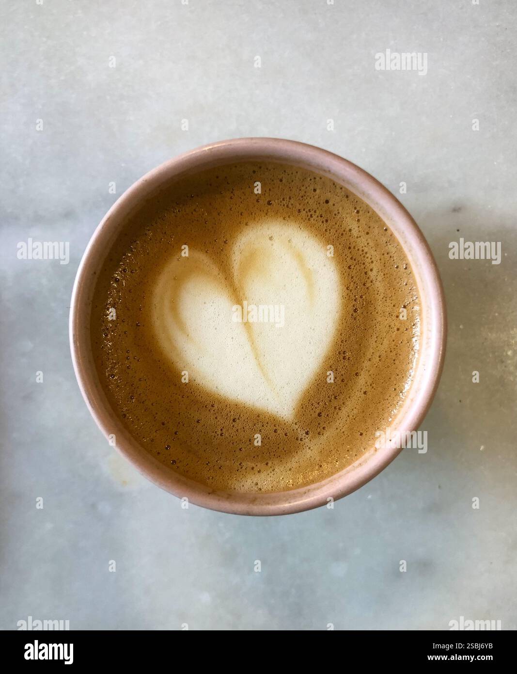 Heart-shaped foam on a steaming hot pink mug of coffee on a white marbled counter. Viewed from directly above. - Smartphone Captured Stock Image