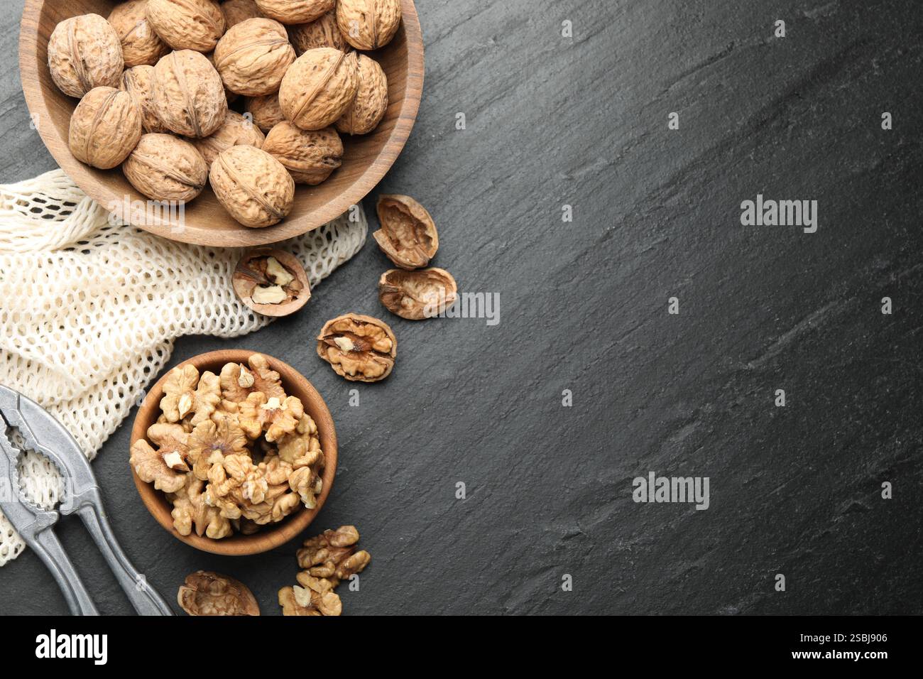 Fresh ripe walnuts, nutcracker and shells on black table, flat lay. Space for text Stock Photo