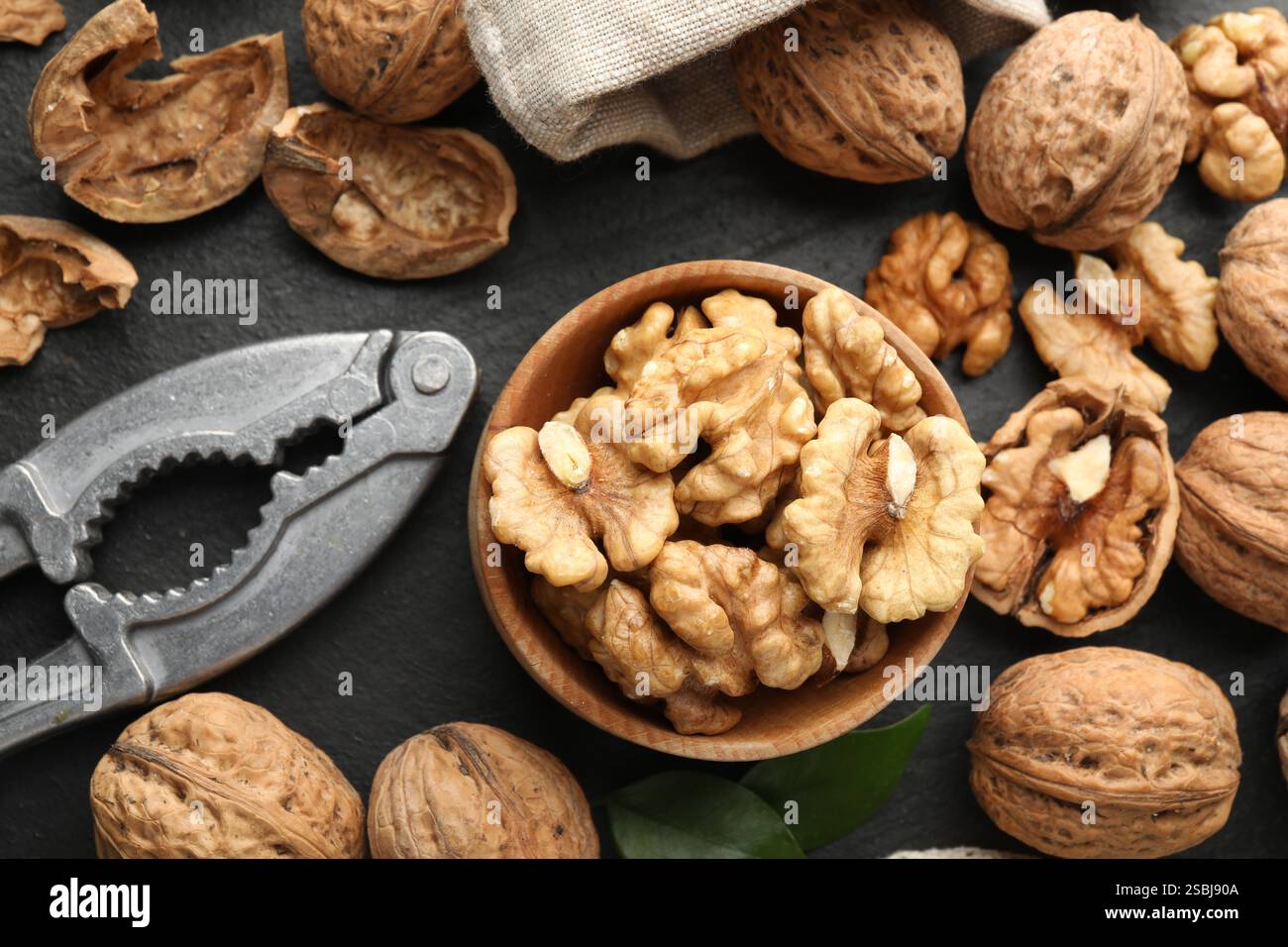 Fresh ripe walnuts, shells and nutcracker on black table, flat lay Stock Photo