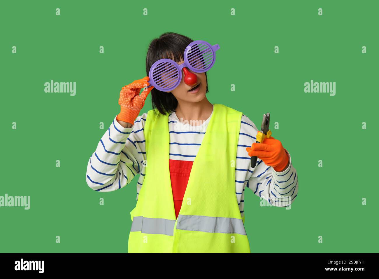 Funny young female builder with pliers on green background. Fool's day Stock Photo