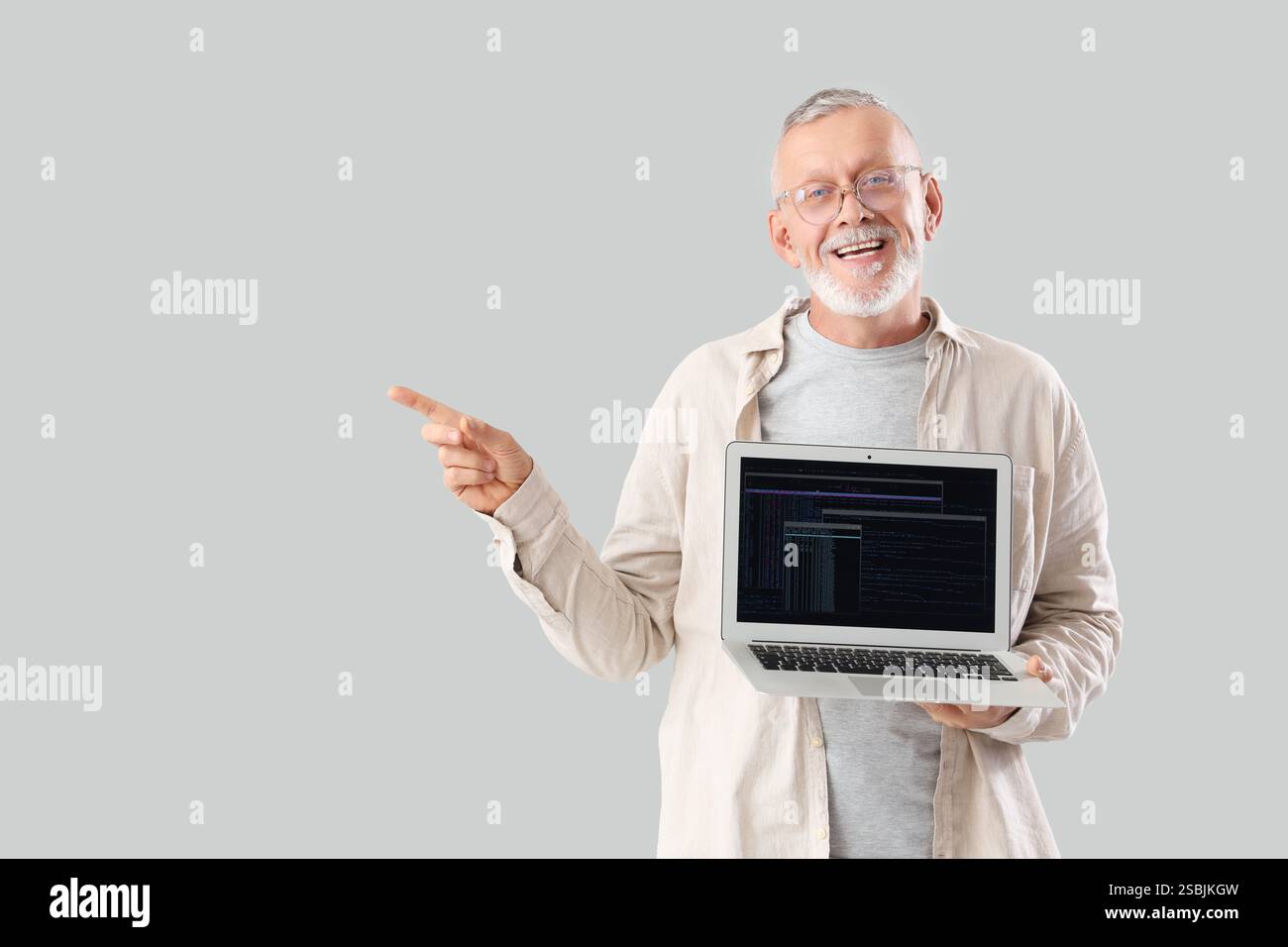 Mature programmer with laptop pointing at something on light background Stock Photo