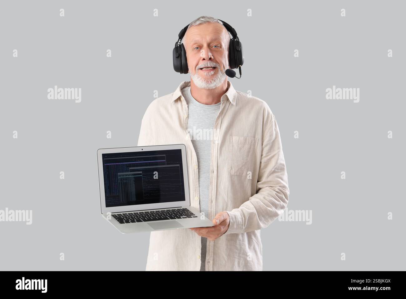 Mature programmer in headset with laptop on light background Stock Photo