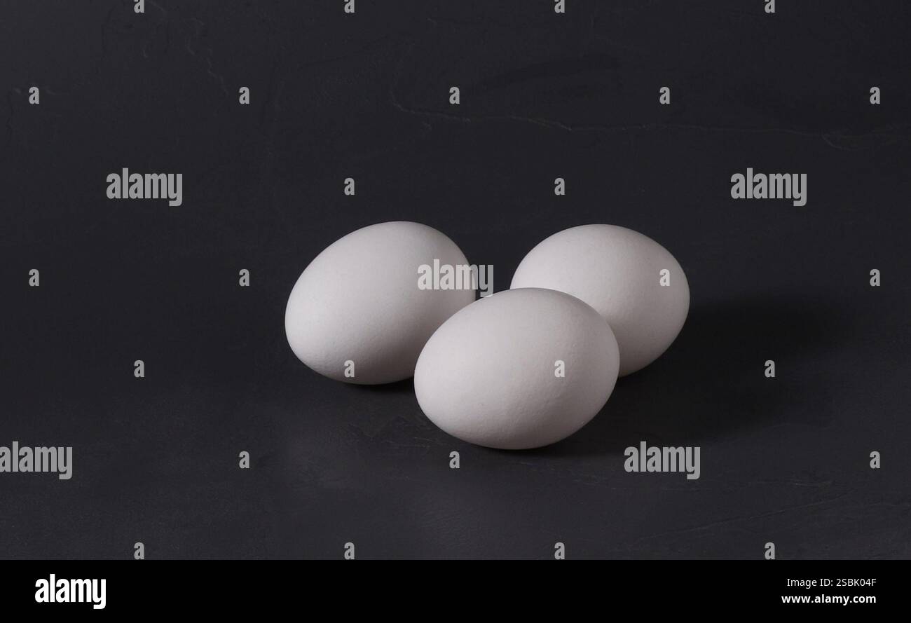 Three white chicken eggs on a dark background. Stock Photo