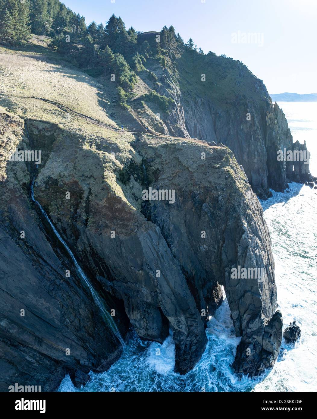 A narrow waterfall flows off a cliff into the ocean along the scenic coastline of northern Oregon. This beautiful area is accessible via highway 101. Stock Photo