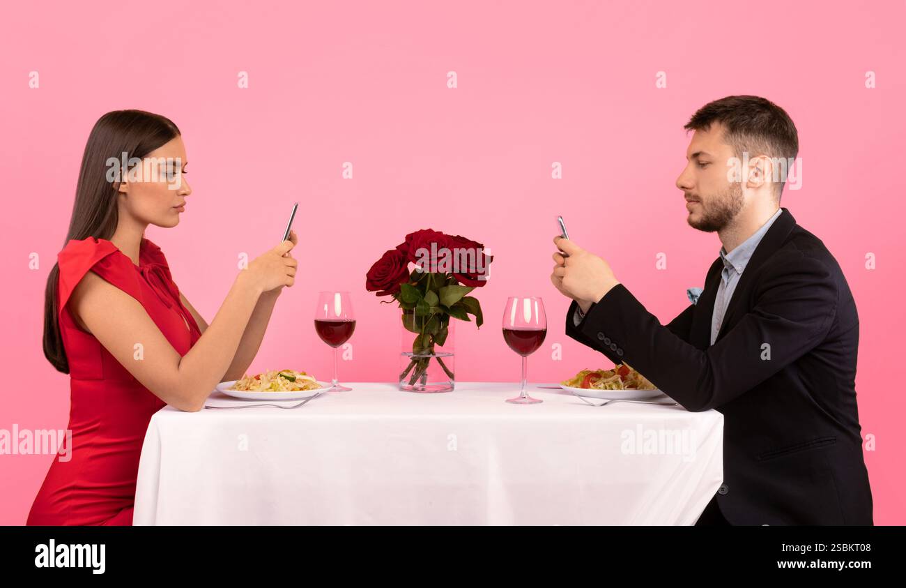 Couple Using Cellphones Sitting At Table Posing Over Yellow Background Stock Photo