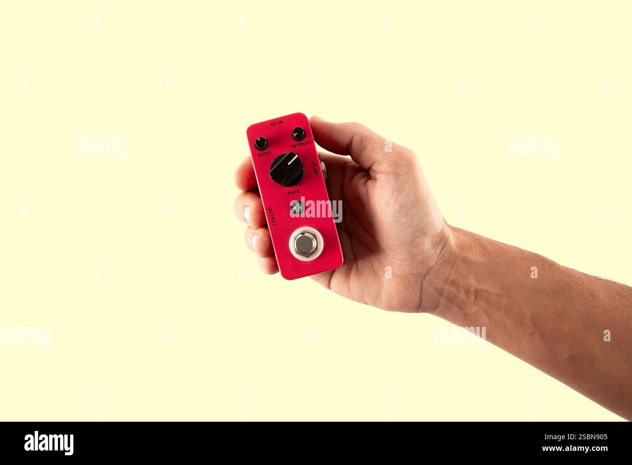 Male hand holding a pink guitar effects pedal isolated on light yellow background cutout Stock Photo