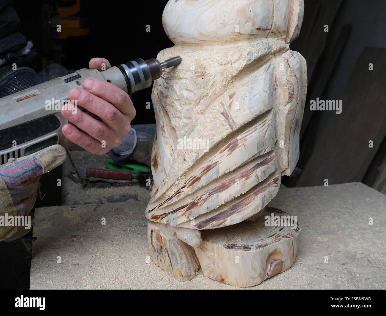 creative woodworking using a drill, cutting out a bird figure from solid wood using a construction hand tool, craftsman's work in a workshop Stock Photo