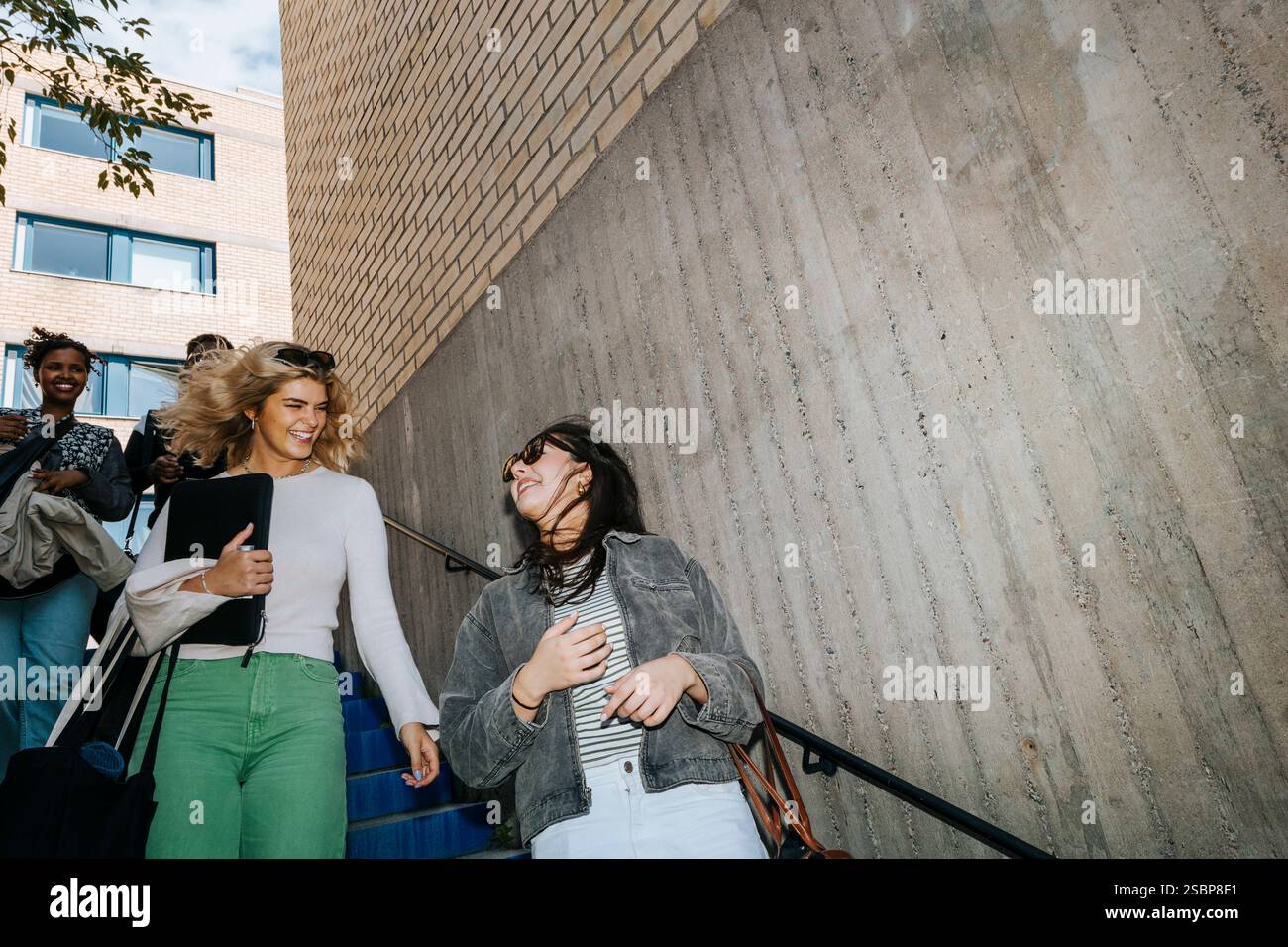 Low angle view of happy female students talking while moving down from stairs Stock Photo