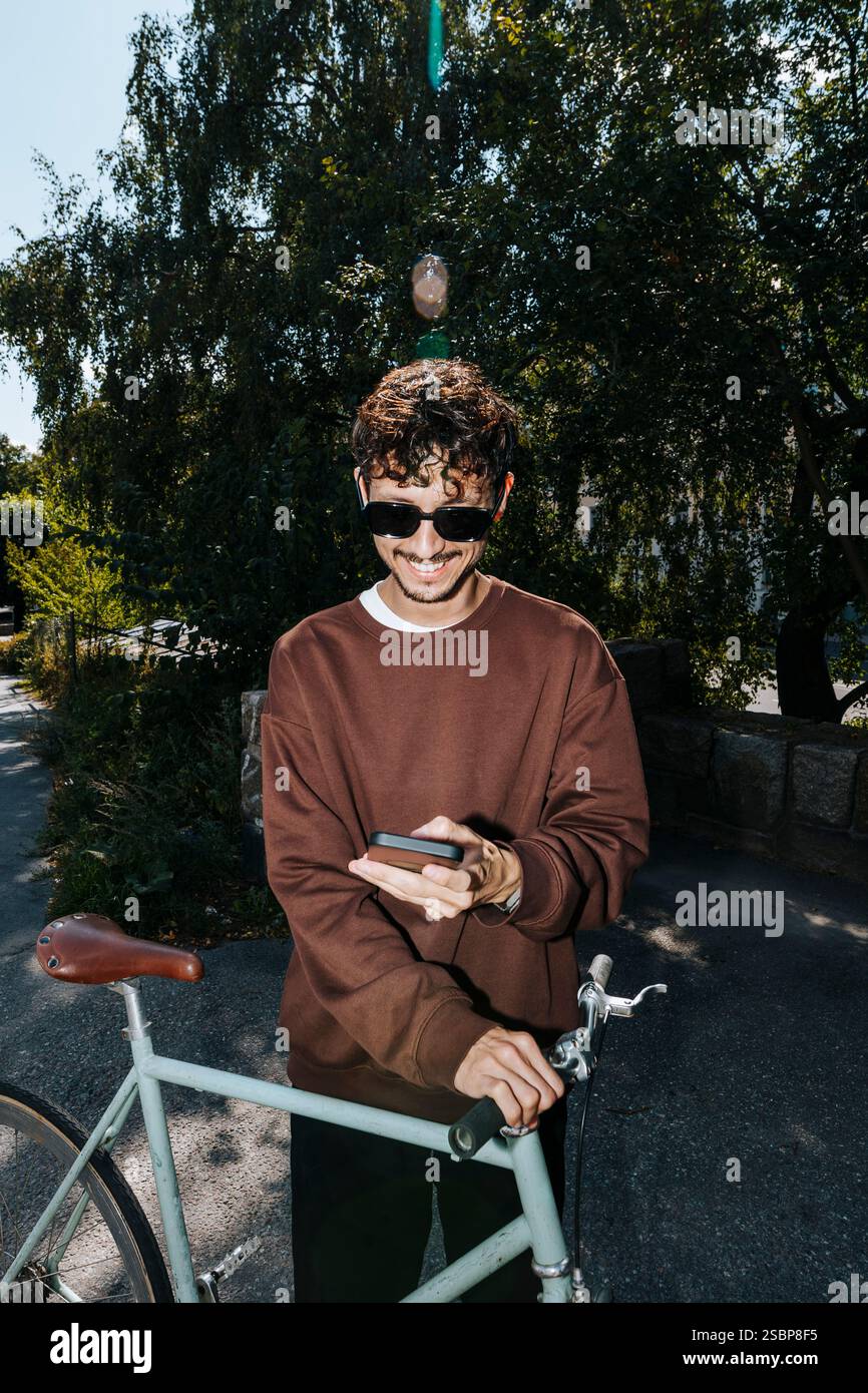 Smiling young man using smart phone while standing with bicycle at park Stock Photo
