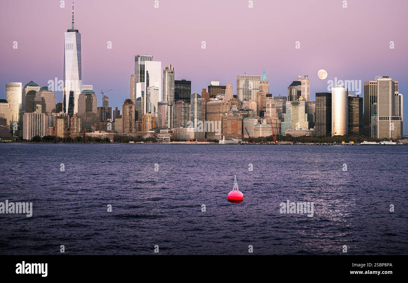 At dusk, the New York City skyline features a glowing full moon and a red buoy on the Hudson River. Stock Photo