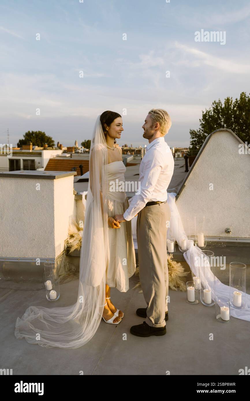 Smiling young married couple holding hands while standing on rooftop Stock Photo
