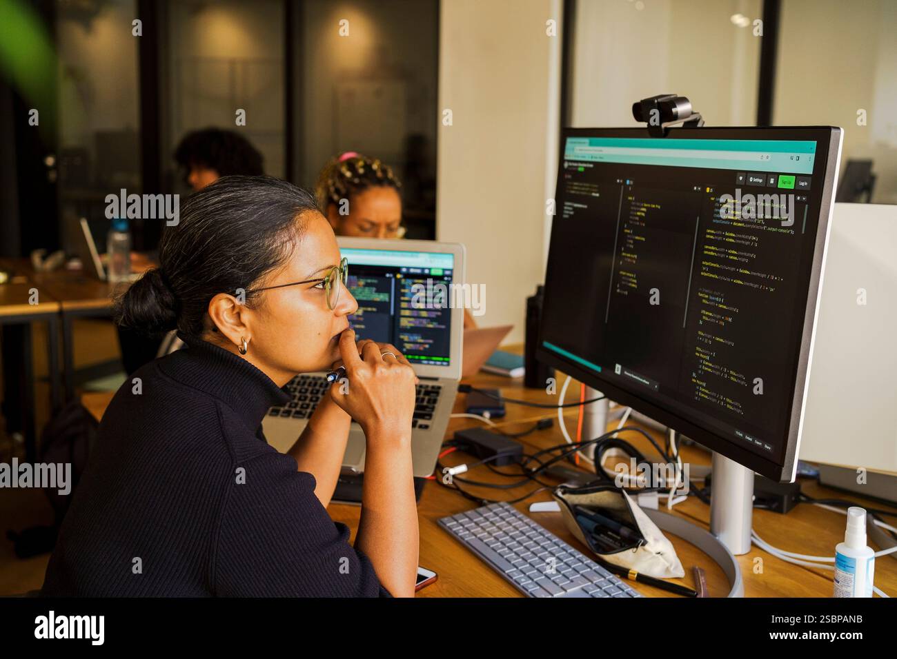 Thoughtful female coder looking at desktop PC while sitting in startup office Stock Photo