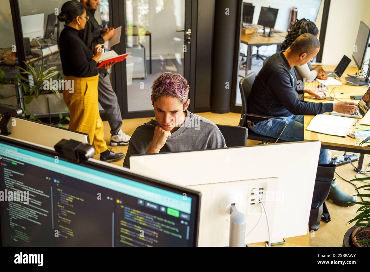 High angle view of focused non-binary computer programmer working on desktop PC in office Stock Photo