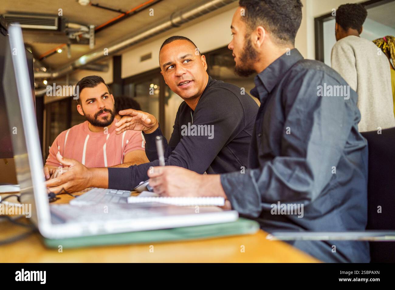 Male computer programmers discussing with each other while sitting at desk in office Stock Photo