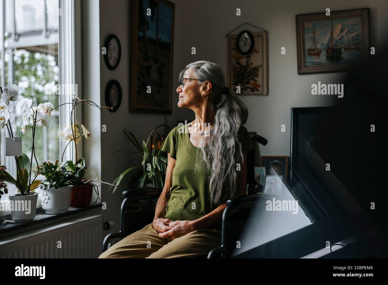 Thoughtful elderly woman looking through window while sitting in wheelchair at nursing home Stock Photo