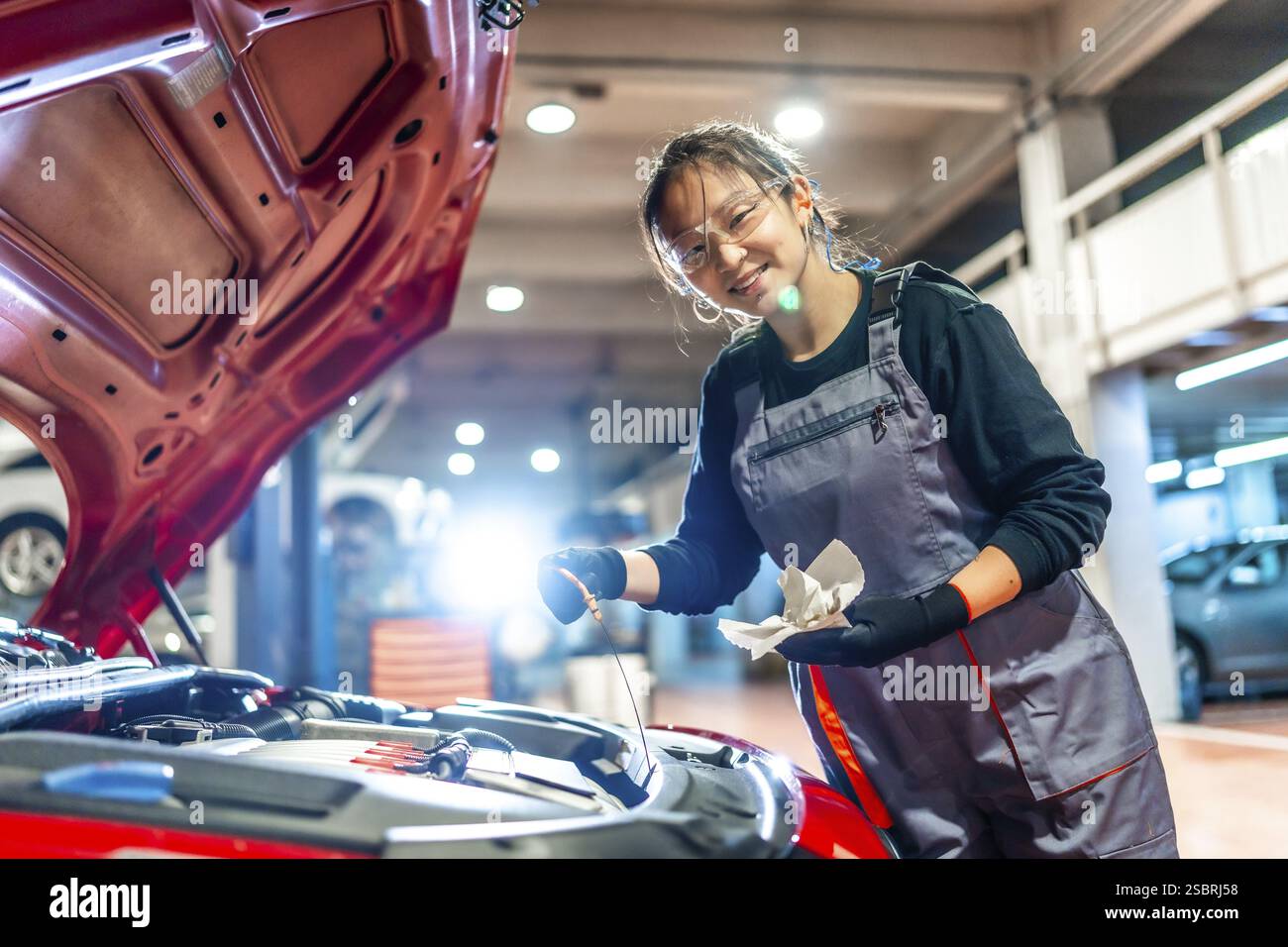 Young female mechanic is checking the oil level of a car engine in a ...