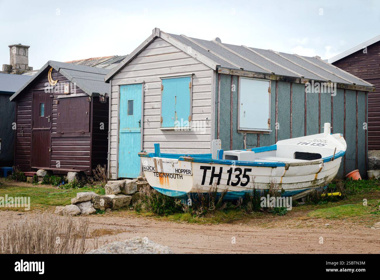 A white rowing boat rests in front of weathered fishing sheds on the ...