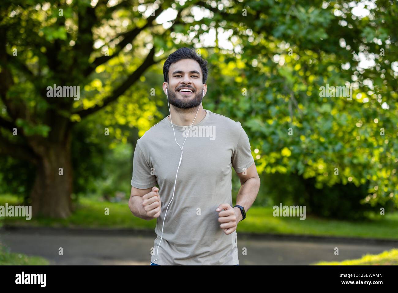 Portrait of a smiling young Indian man wearing headphones doing sports and doing a morning jog in the park. Stock Photo