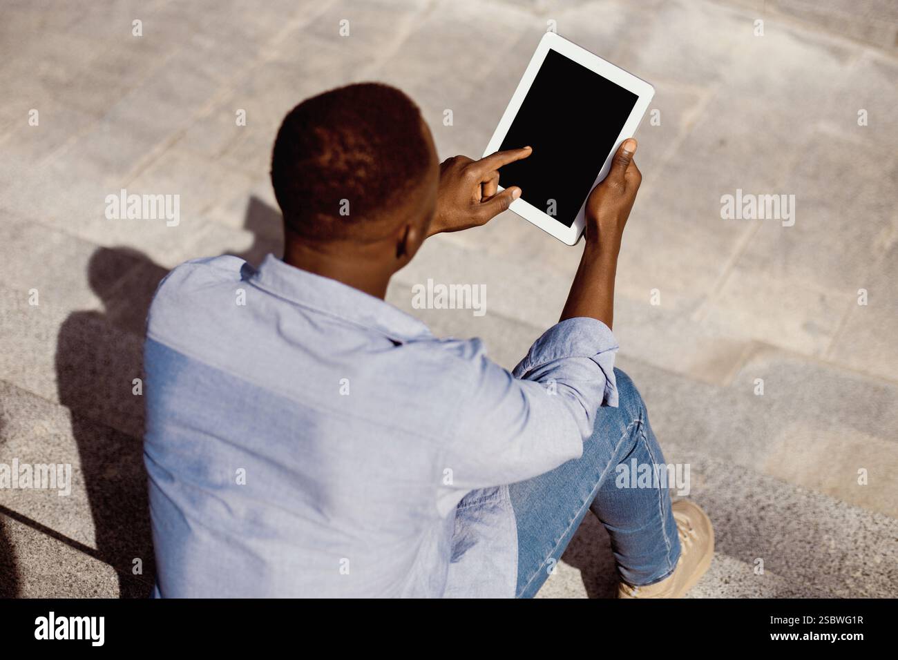 Guy Using Tablet Young black guy using tablet computer with empty screen on stone stairs ...