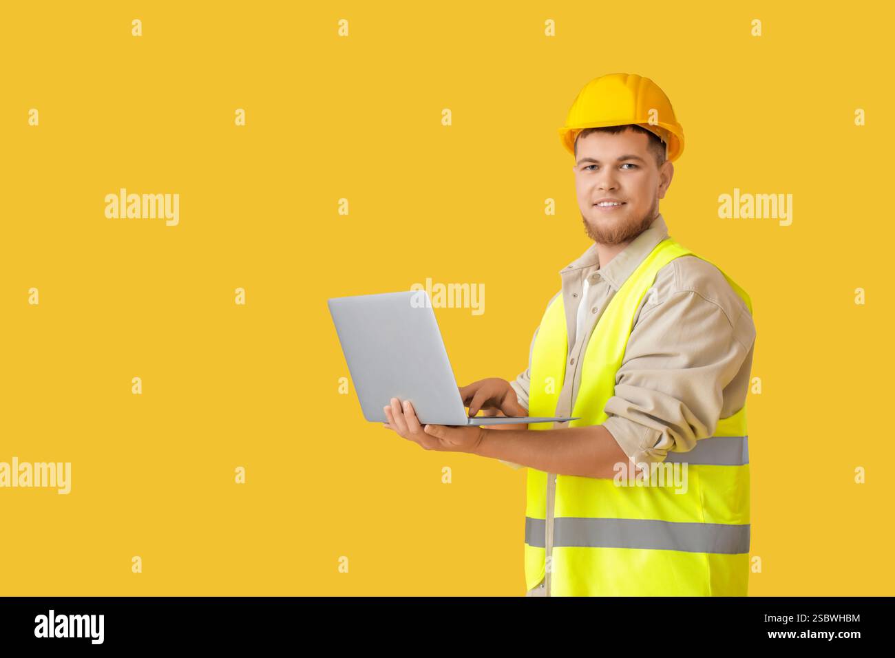 Male contractor using laptop on yellow background Stock Photo