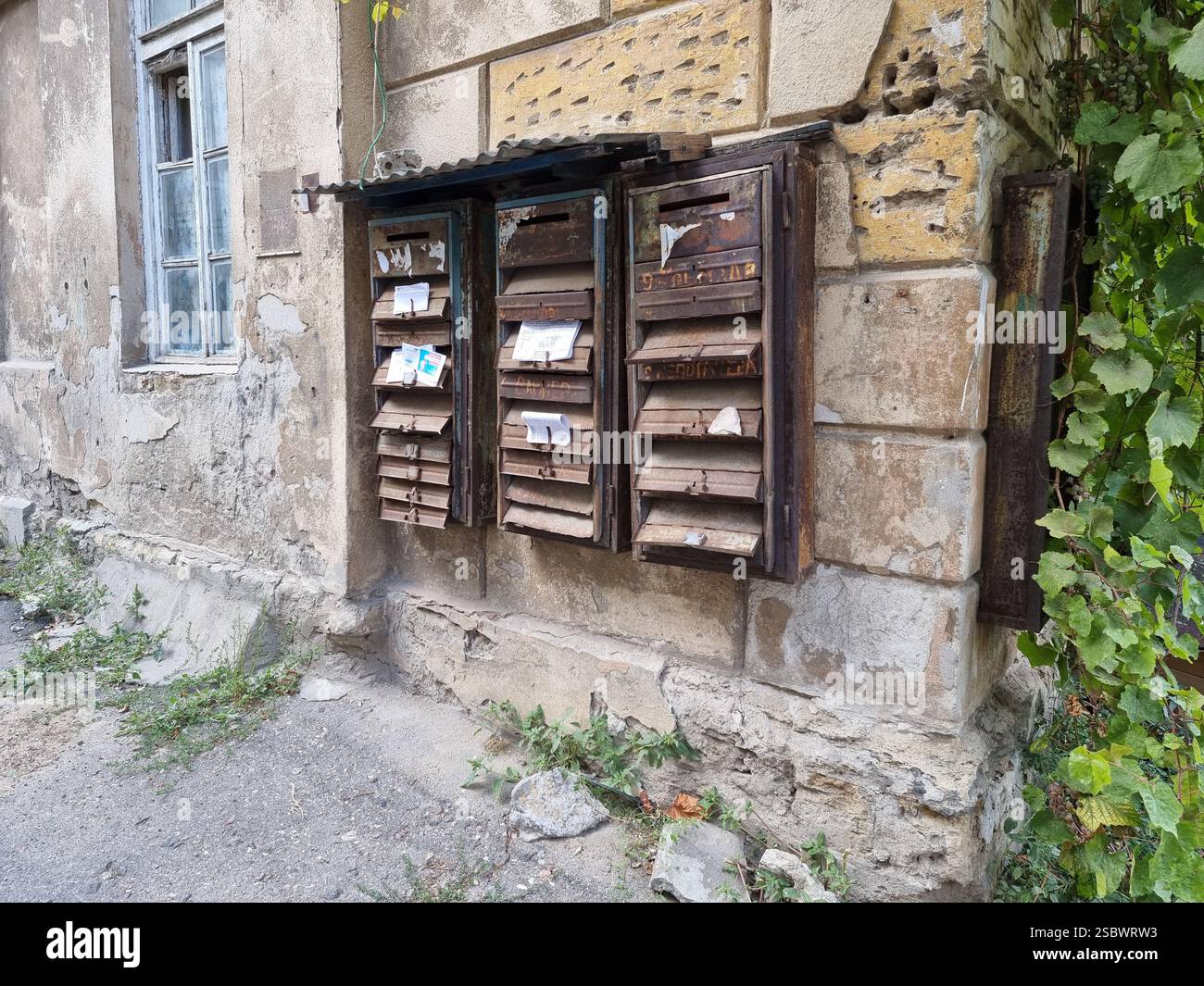 Group of old rusty mailboxes on the weathered stone wall of a residential building - Smartphone Captured Stock Image