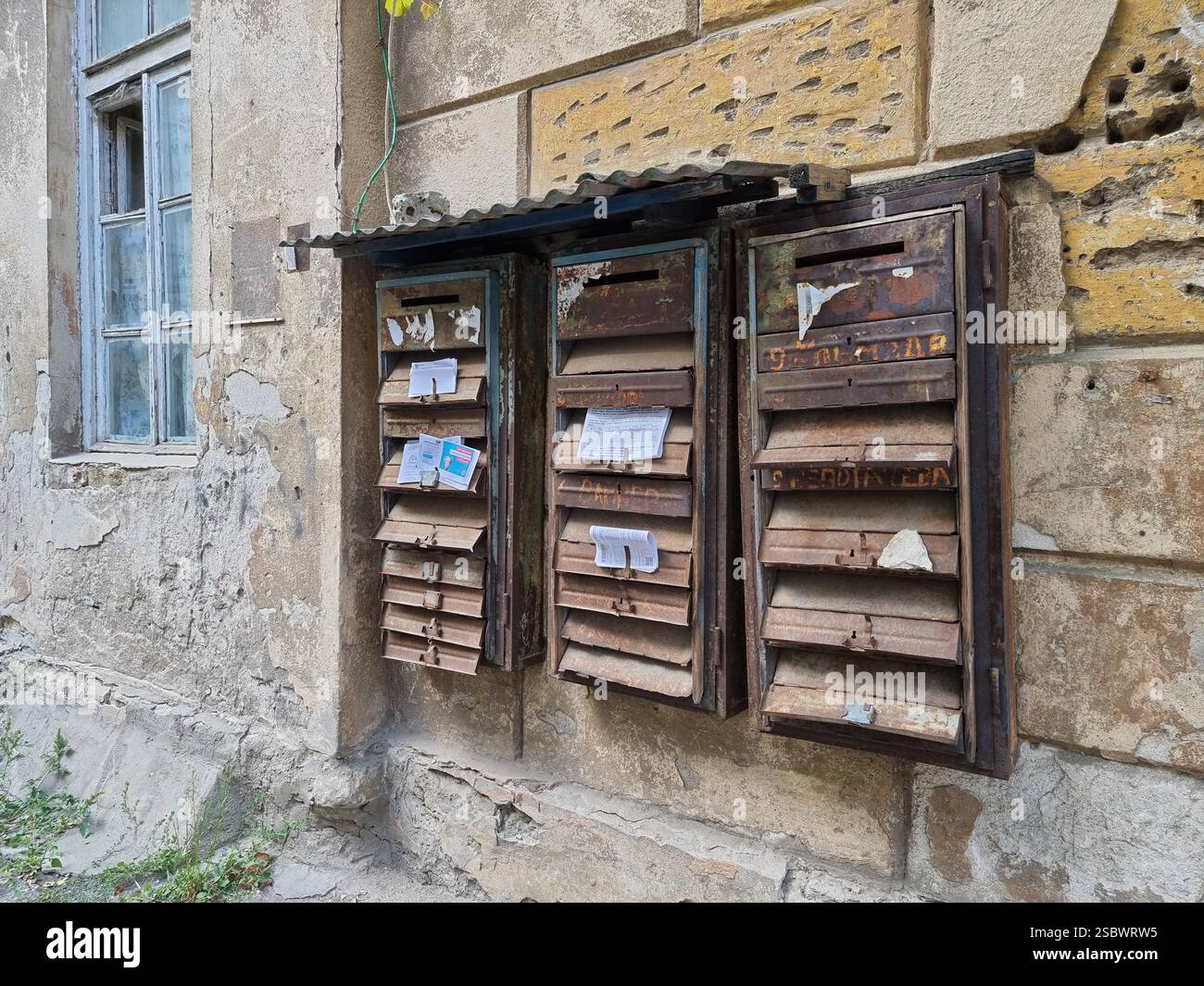 Group of old rusty mailboxes on the weathered stone wall of a residential building - Smartphone Captured Stock Image