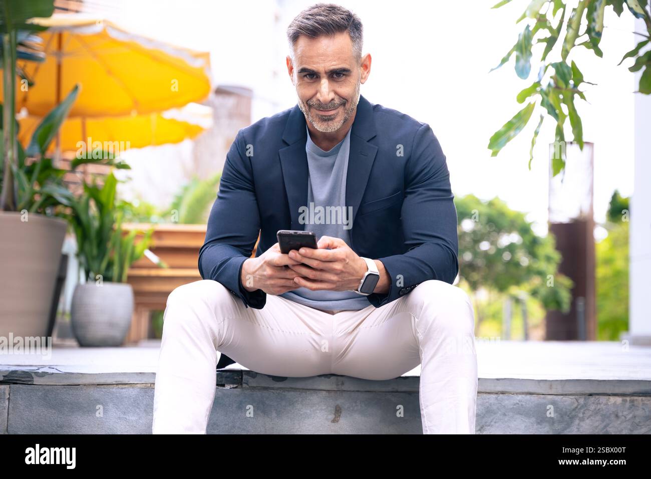 Smiling Man Using Smartphone While Sitting Outdoors in Urban Setting Stock Photo