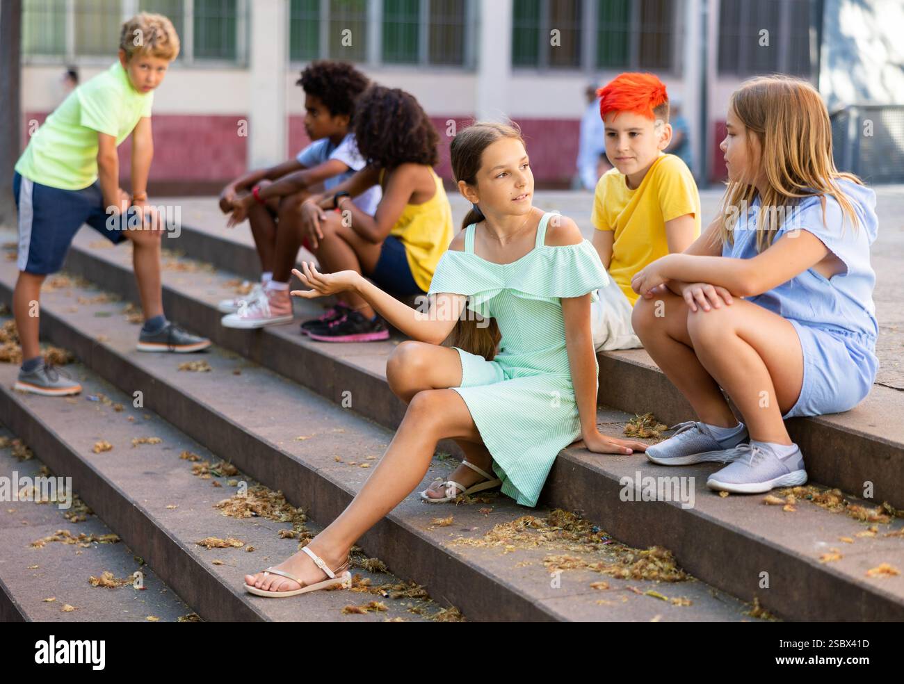 Happy tweenagers friends sitting on steps outdoors and chatting Stock Photo