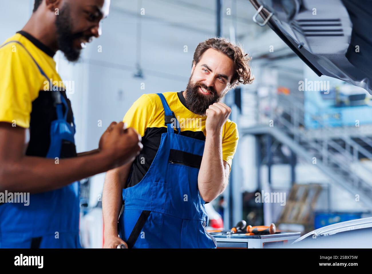 Repairmen in auto repair shop working together on fixing car, excited ...