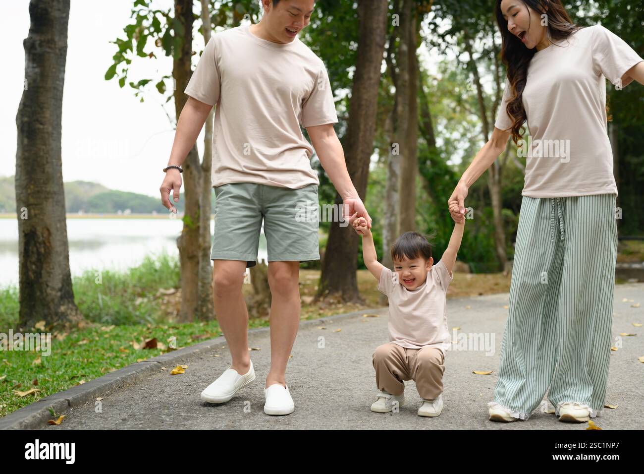 Parents holding their toddler hands while walking along a park path ...
