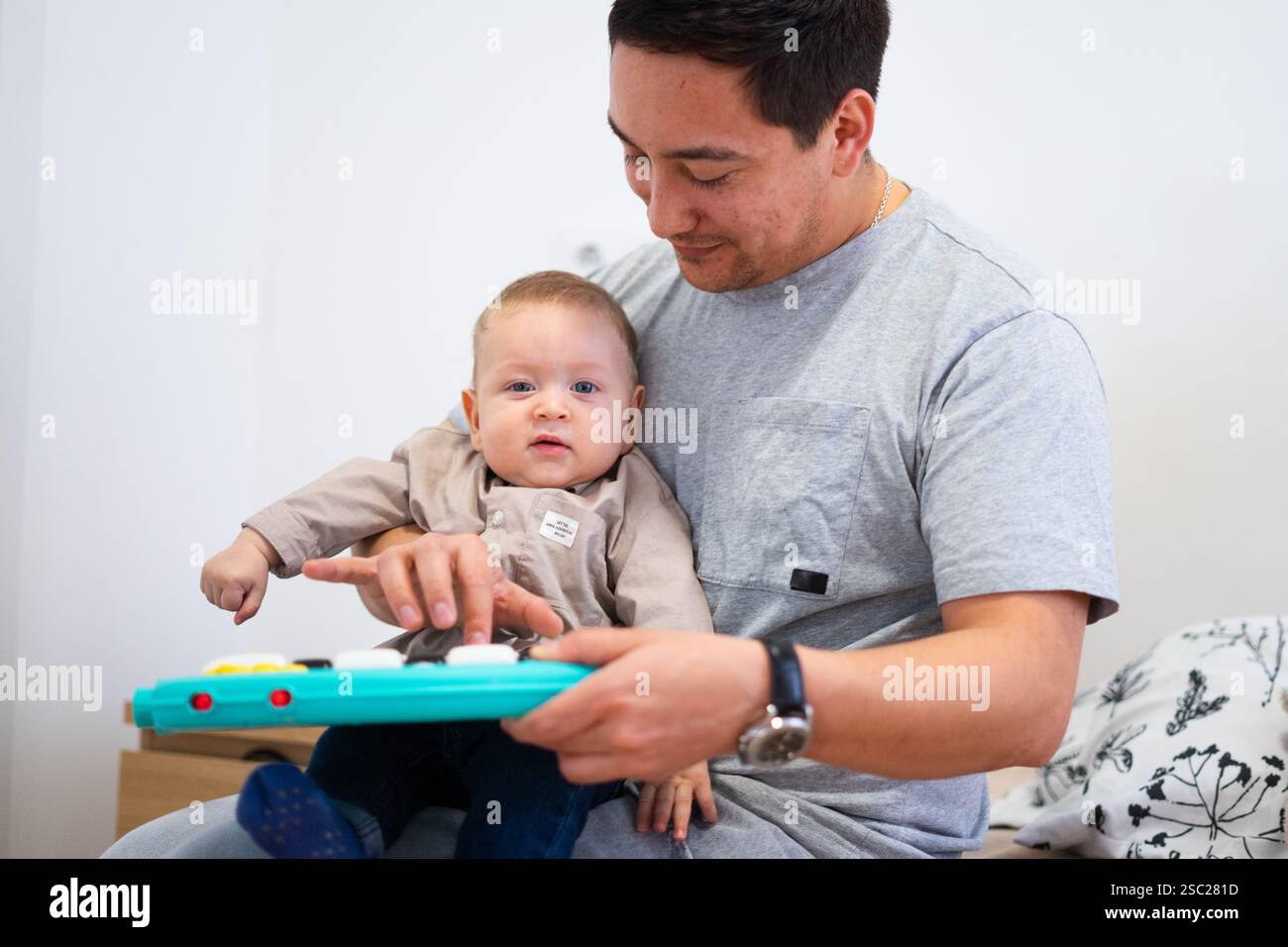 Dad holding his baby boy and playing a toy piano together, enjoying