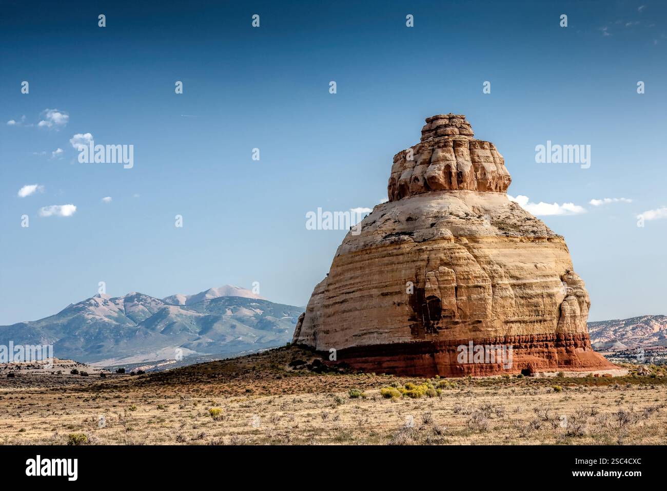 A large rock formation sits in the middle of a desert. The sky is clear ...
