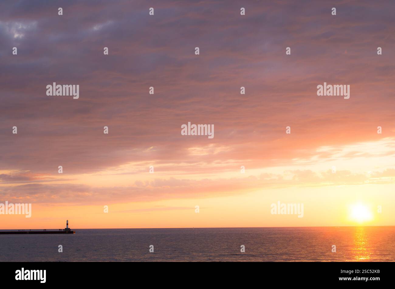 Serene sunset over Lake Michigan with a lighthouse on the pier, casting a golden glow on the calm waters and sky. Stock Photo