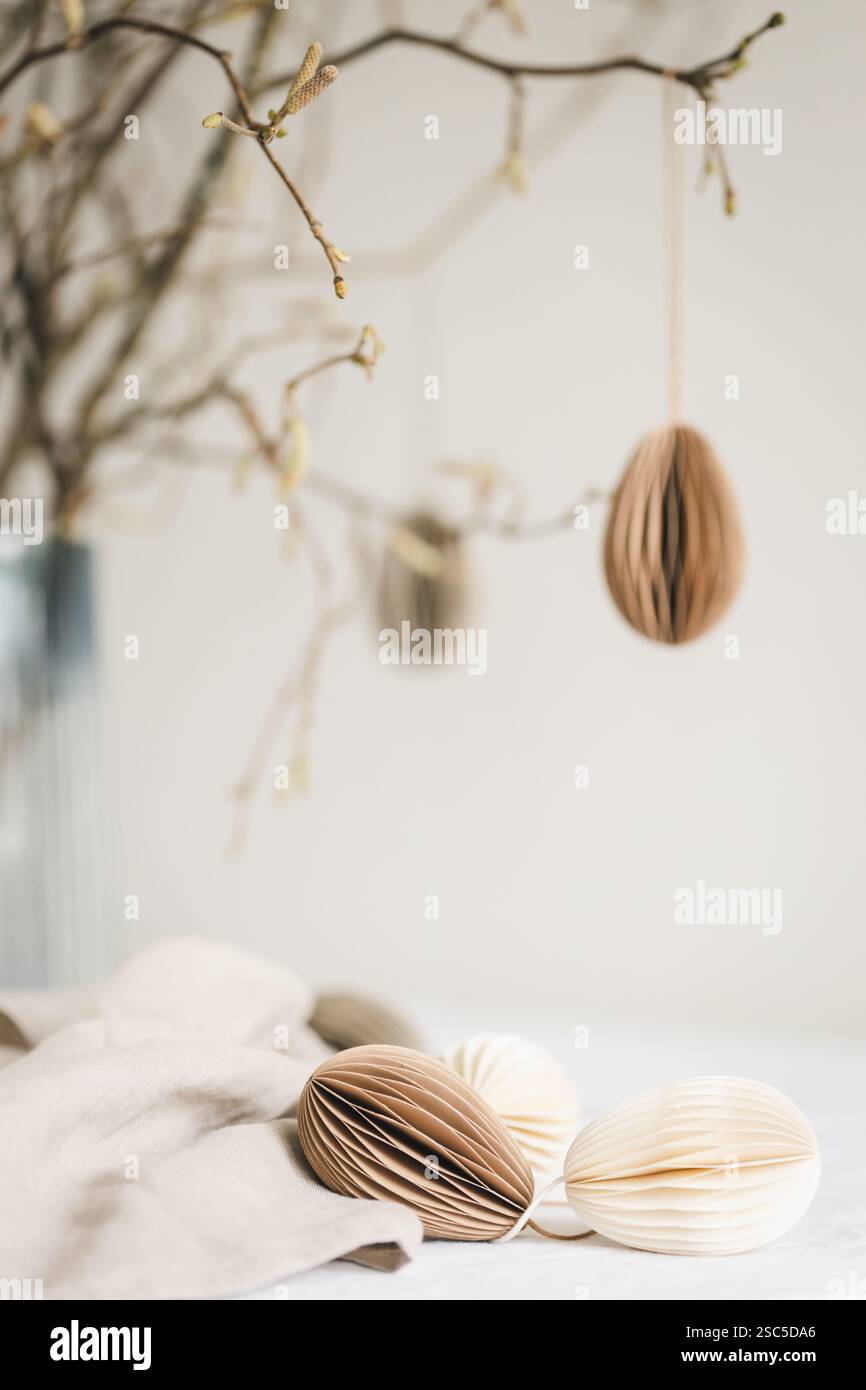 Paper Easter eggs hanging on branches under table with decorations on it. Stock Photo