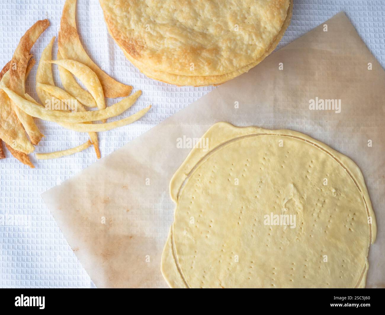 Cooking of a shortcrust puff pastry Napoleon cake with a pile of baked thin buttery layers, a raw layer rolled out on a baking paper and dough scraps Stock Photo