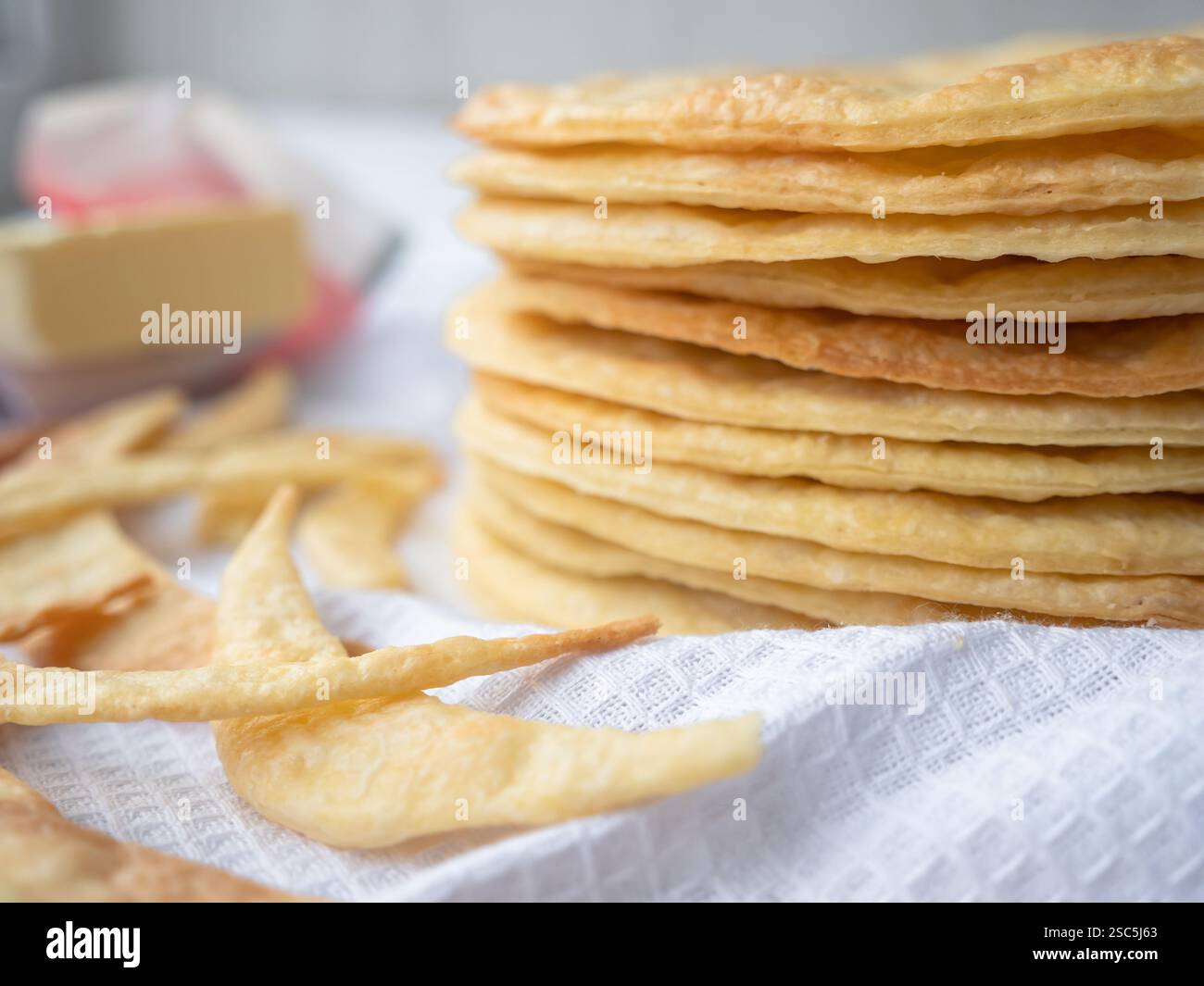 A pile of baked thin round buttery layers, dough scraps and butter on a white waffle towel ready to make a shortcrust puff pastry Napoleon cake. Stock Photo