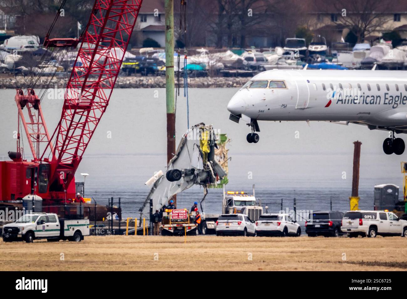 An aircraft lands as a crane offloads a piece of wreckage from a ...