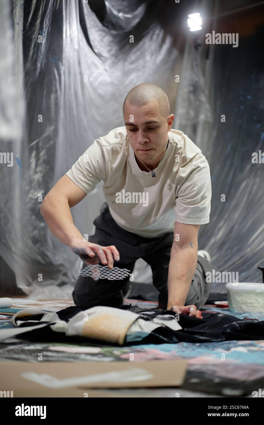 Concentrated Male Artist Removing Grid Stencil Pattern From Fabric