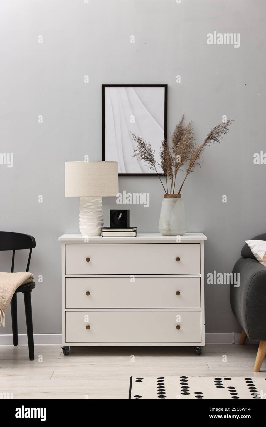 Dresser with lamp and decor near light grey wall in room. Interior ...