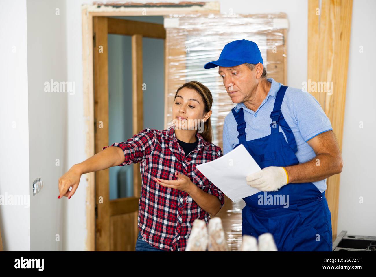 View of Man worker talking with woman owner of apartment about renovation works ...