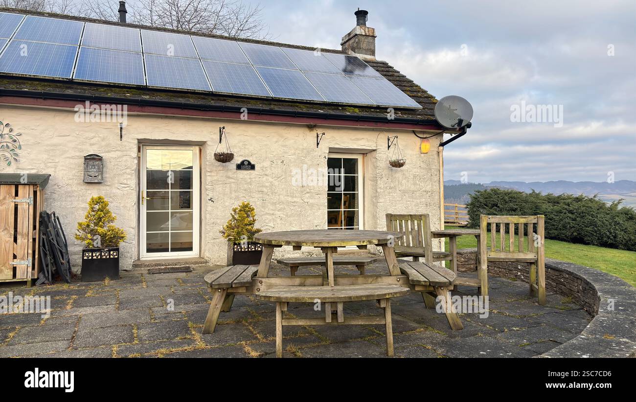 Traditional Scottish farm cottage with solar panels on the roof. White painted stone. Garden aspect. Modern croft - Smartphone Captured Stock Image