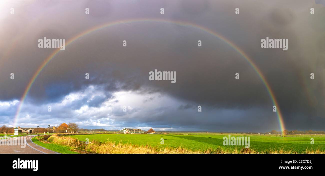 A vibrant rainbow arches over a green landscape under a dramatic sky ...