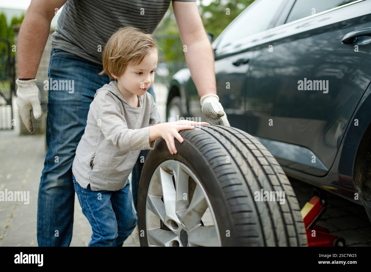 Using Children Wheel Cute little boy helping his father to change car wheels at their ...