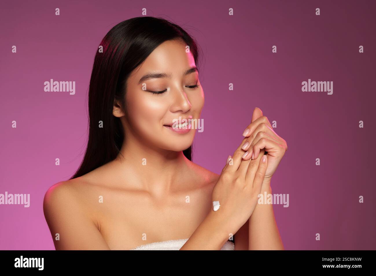 Beauty routine featuring a woman applying cream in a studio with pink ...