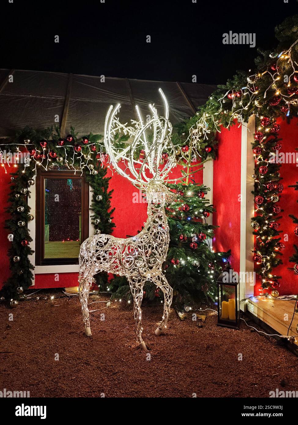 LED figure deer outdoor. New Year Christmas Decoration LED Figure Deer near Christmas tree. Figure of a deer on a wire frame, decorated with a luminous garland at night. Light Deer LED garland bulbs. Stock Photo