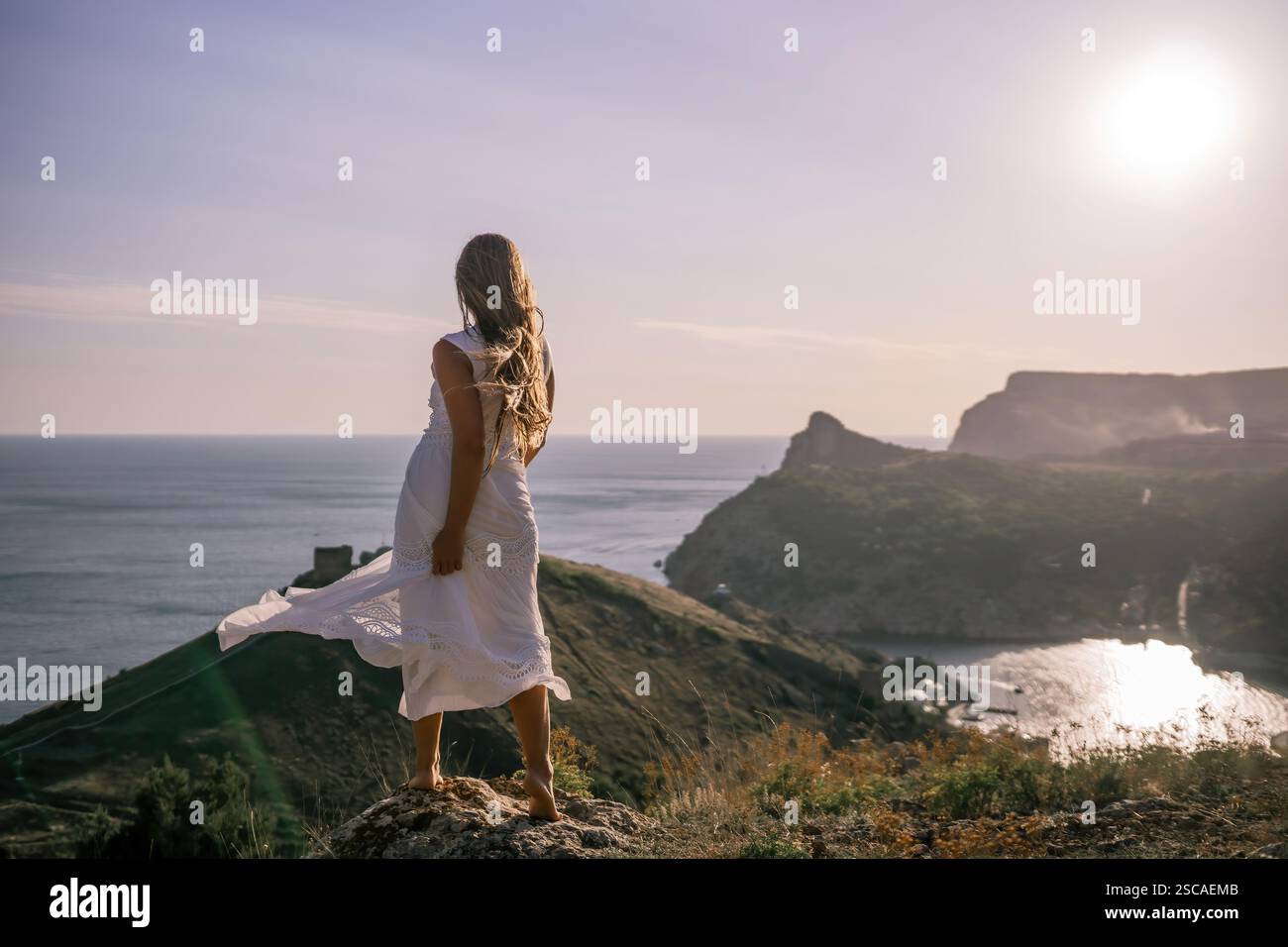 A woman in a white dress stands on a hill overlooking the ocean. The ...