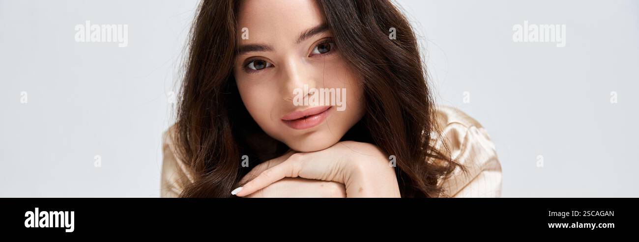 A young woman with long hair gazes thoughtfully while resting her chin ...
